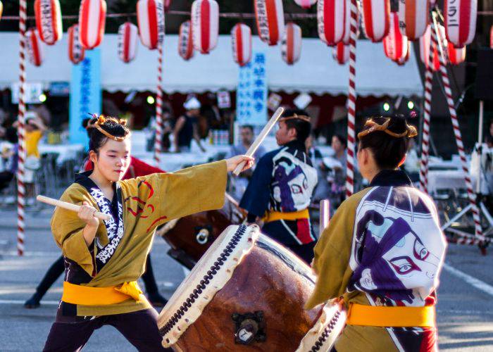 Performers at an Obon Odori hitting taiko drums under paper lanterns.